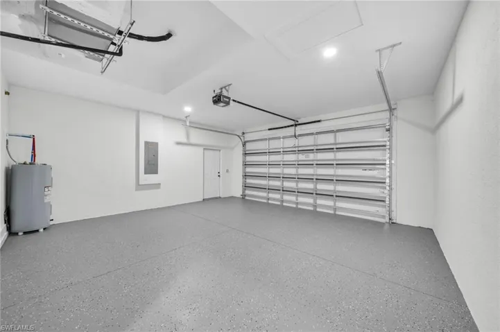 Garage with water heater, electric panel, and a garage door opener