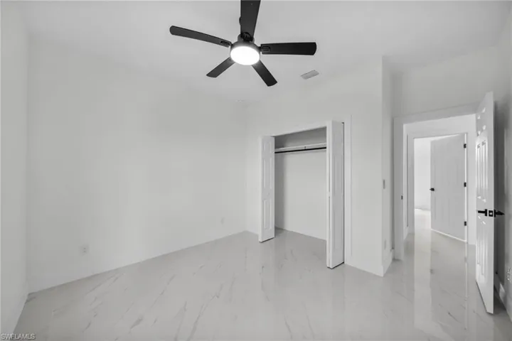 Unfurnished bedroom featuring light marble finish floors, a ceiling fan, and a closet