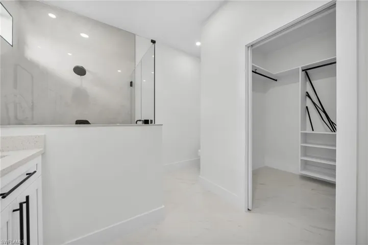 Bathroom featuring a walk in closet, light marble finish flooring, a marble finish shower, vanity, and recessed lighting