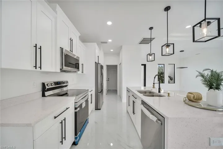 Kitchen with appliances with stainless steel finishes, white cabinets, hanging light fixtures, light marble finish floors, and light stone countertops
