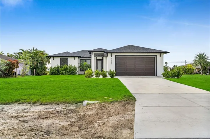 Prairie-style home featuring a front yard, stucco siding, driveway, an attached garage, and a shingled roof