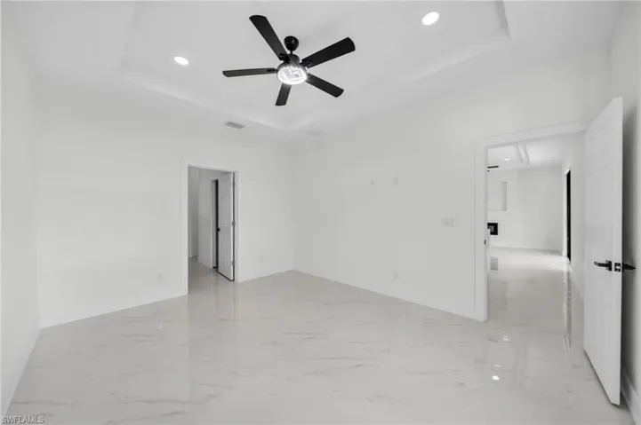Unfurnished room with a raised ceiling, recessed lighting, light marble finish floors, a ceiling fan, and attic access