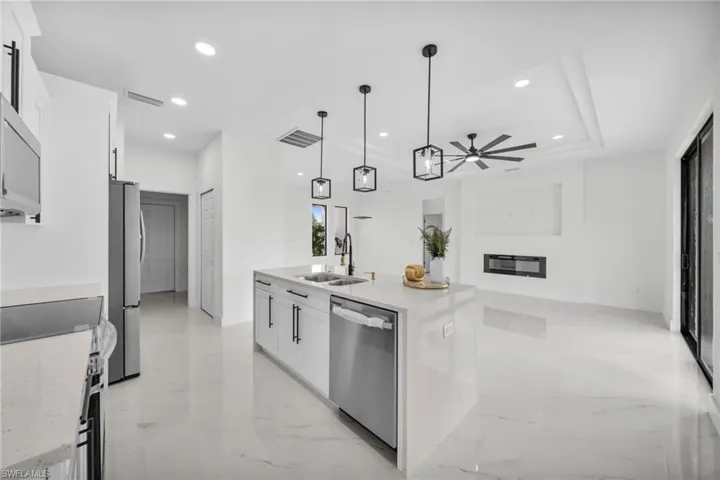 Kitchen with white cabinets, light stone countertops, light marble finish floors, hanging light fixtures, and stainless steel appliances