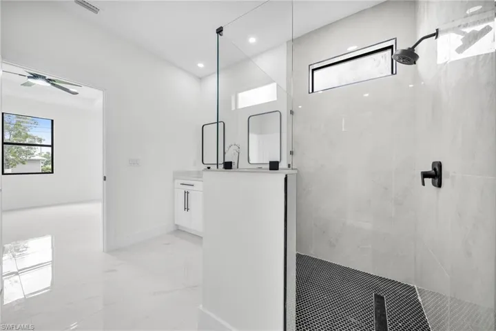 Bathroom with vanity, a marble finish shower, light marble finish floors, and recessed lighting