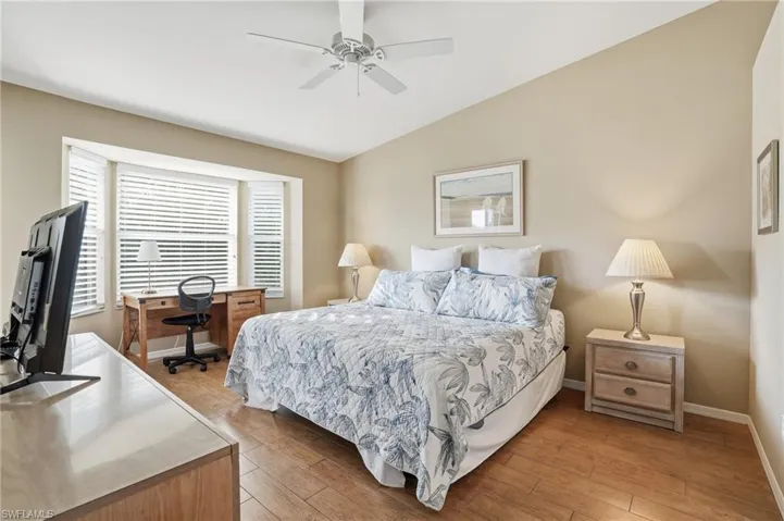 Bedroom with an office area, light wood-type flooring, vaulted ceiling, and ceiling fan
