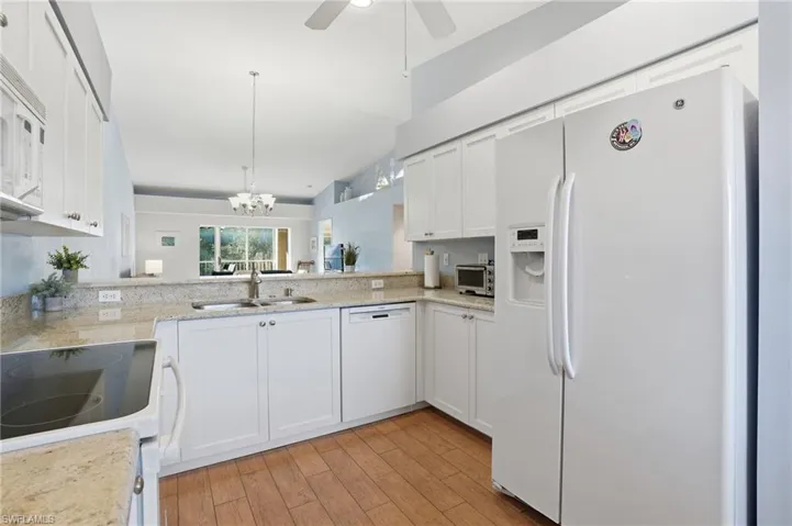 Kitchen featuring white cabinets, white appliances, a chandelier, light stone counters, and light wood-style floors