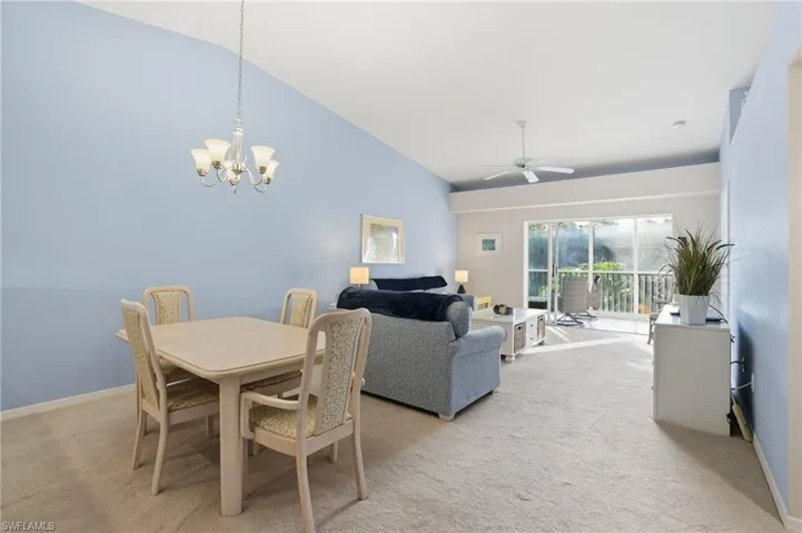 Dining room featuring vaulted ceiling, light carpet, a chandelier, and a ceiling fan