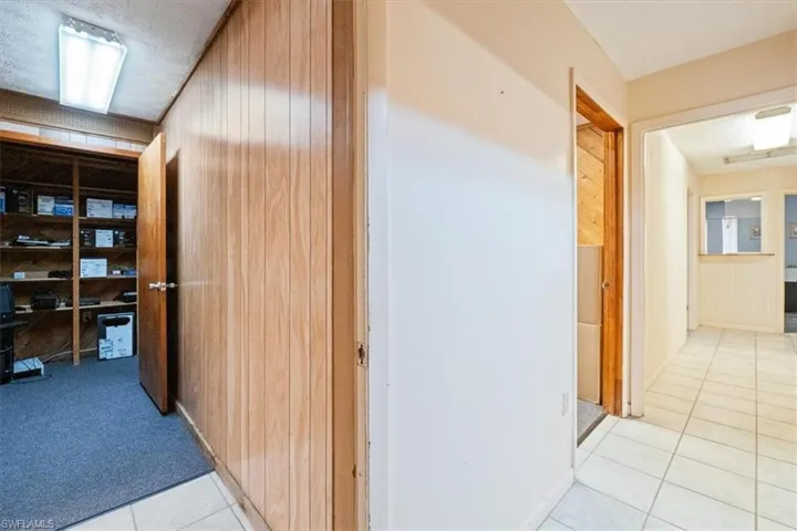 Hall featuring a textured ceiling, wood walls, light tile patterned flooring, and a desk