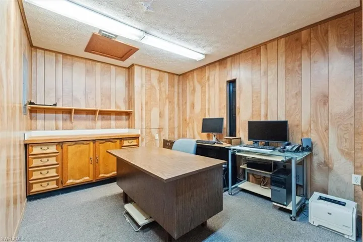 Office area with wood walls, dark carpet, and a textured ceiling