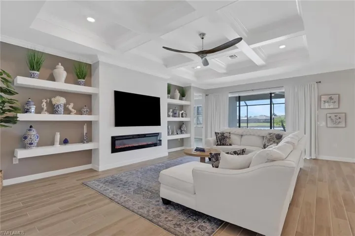 Living area featuring a large fireplace, wood tiled floors, built in shelves, ceiling fan, and coffered ceiling