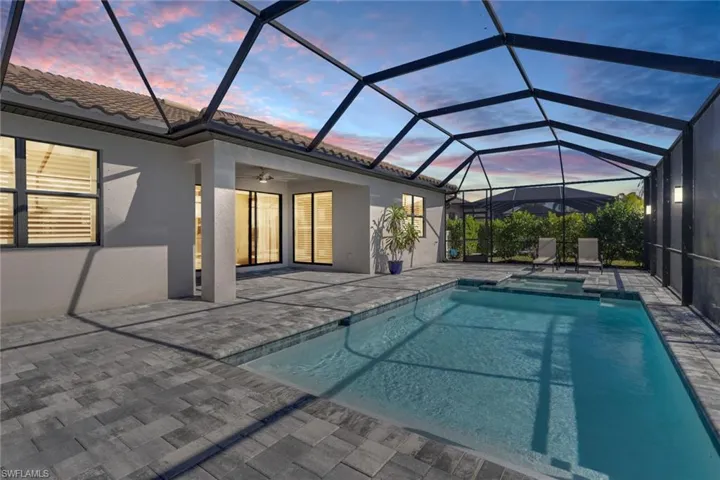 Pool at dusk with a sunroom, a lanai, a patio, and a pool with connected hot tub