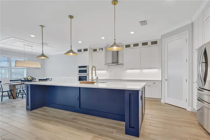 Kitchen with white cabinetry, hanging light fixtures, wood finish floors, a center island with sink, and crown molding