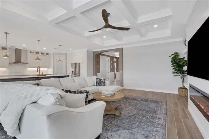 Living room featuring wood finish floors, coffered ceiling, beamed ceiling, crown molding, and recessed lighting