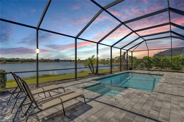 View of pool featuring a sunroom, a pool with connected hot tub, a water view, and glass enclosure