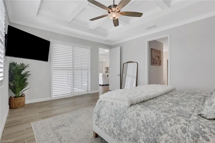Bedroom with wood finish floors, coffered ceiling, ornamental molding, a ceiling fan, and beamed ceiling