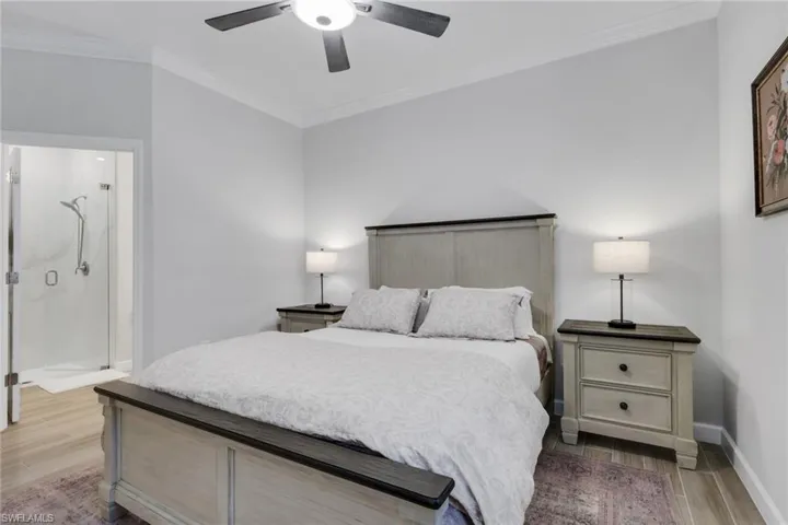 Bedroom with ornamental molding, light wood-type flooring, ceiling fan, and ensuite bathroom