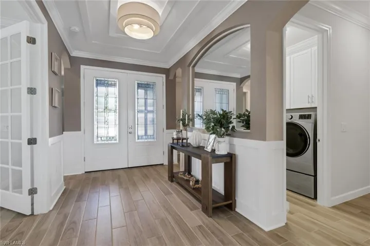 Foyer entrance with wainscoting, ornamental molding, wood finish floors, washer / clothes dryer, and french doors