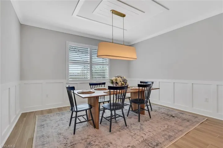 Dining area with wainscoting, crown molding, a decorative wall, and light wood-style floors