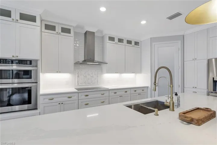 Kitchen featuring wall chimney exhaust hood, stainless steel appliances, white cabinets, glass insert cabinets, and tasteful backsplash