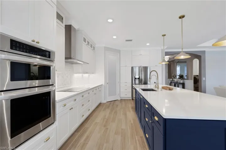 Kitchen featuring appliances with stainless steel finishes, white cabinetry, blue cabinets, arched walkways, and glass insert cabinets