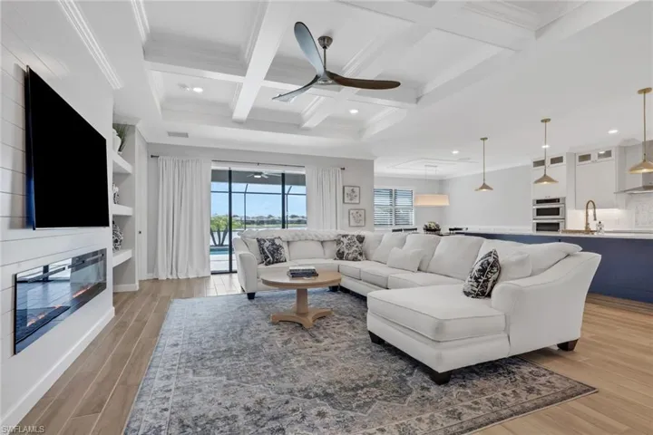 Living room featuring a large fireplace, ceiling fan, coffered ceiling, healthy amount of natural light, and beam ceiling