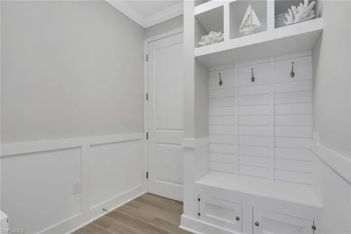 Mudroom with a wainscoted wall, wood finish floors, a decorative wall, and crown molding