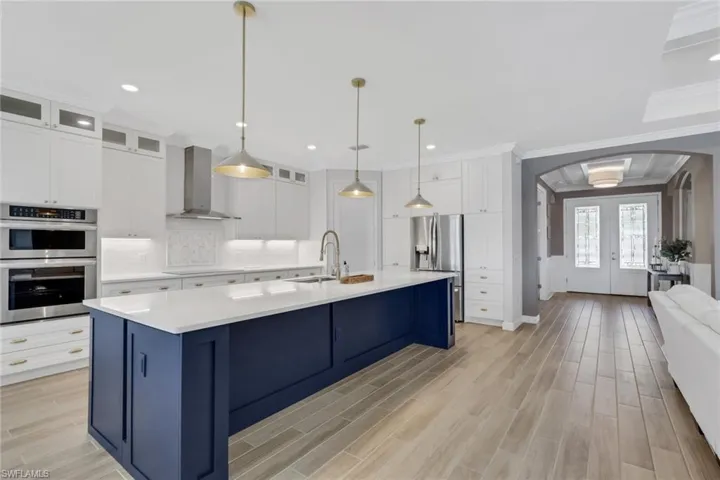 Kitchen with arched walkways, blue cabinets, stainless steel appliances, wall chimney exhaust hood, and white cabinetry