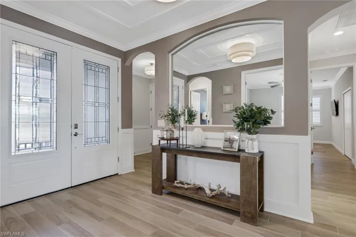 Entrance foyer with arched walkways, wood tiled floors, ornamental molding, wainscoting, and french doors