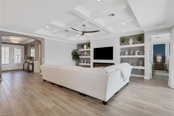 Living room with crown molding, arched walkways, light wood finished floors, coffered ceiling, and built in features
