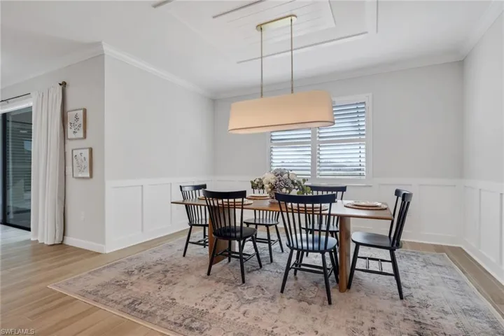 Dining room with crown molding, wainscoting, a decorative wall, and light wood-style floors