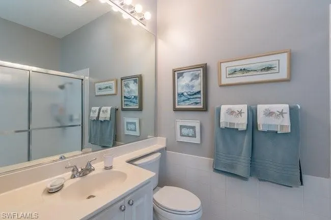 Bathroom featuring tile walls, vanity, toilet, and an enclosed shower