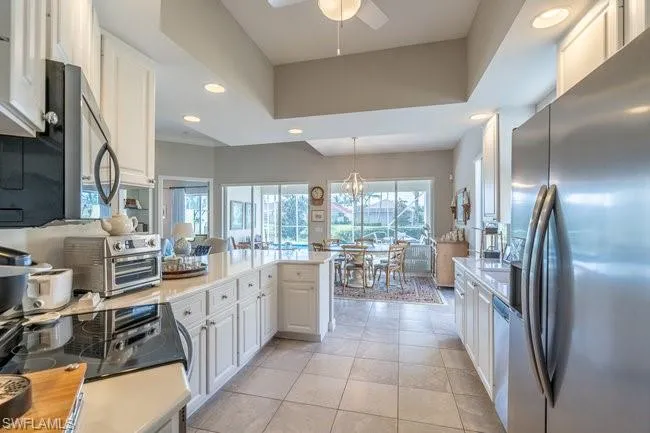 Kitchen with light tile patterned floors, decorative light fixtures, white cabinetry, stainless steel appliances, and ceiling fan with notable chandelier