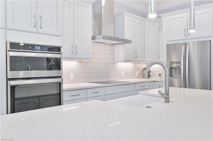 Kitchen featuring ornamental molding, white cabinets, appliances with stainless steel finishes, and wall chimney range hood