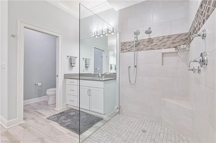 Bathroom with a tile shower, ornamental molding, vanity, and toilet