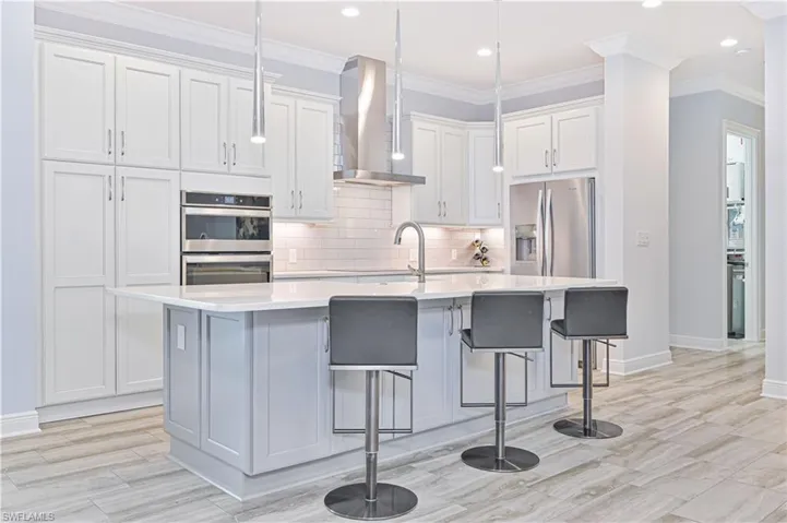 Kitchen with an island with sink, white cabinets, wall chimney exhaust hood, stainless steel appliances, and a kitchen bar
