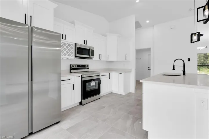 Kitchen with stainless steel appliances, white cabinets, hanging light fixtures, light stone counters, and recessed lighting