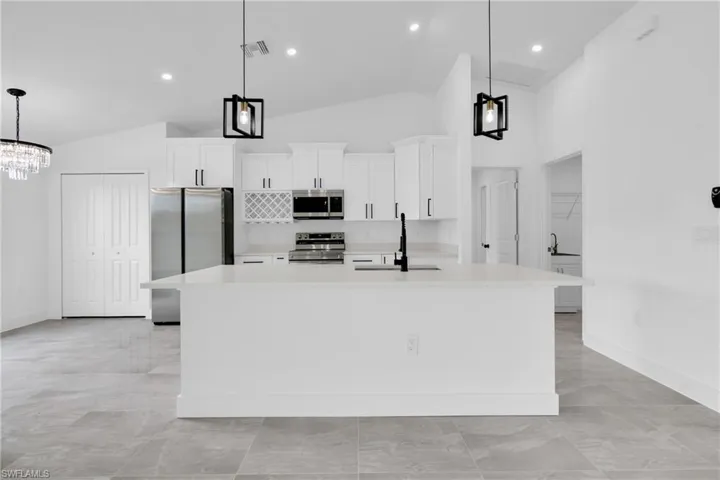Kitchen featuring hanging light fixtures, appliances with stainless steel finishes, white cabinets, a center island with sink, and light stone countertops