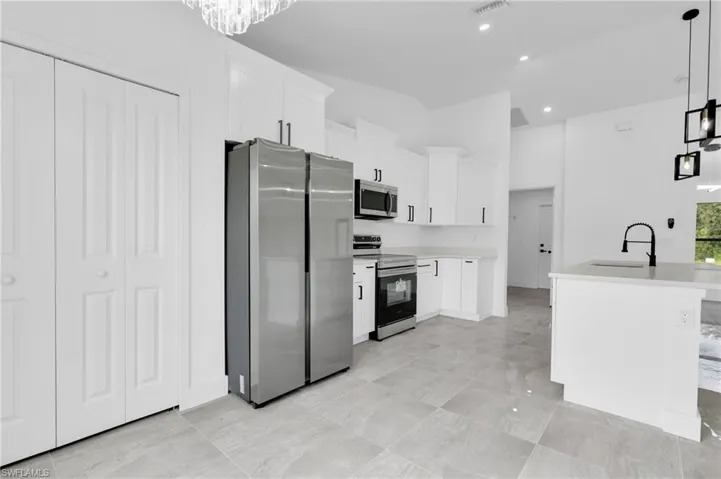 Kitchen featuring pendant lighting, appliances with stainless steel finishes, white cabinets, recessed lighting, and a center island with sink