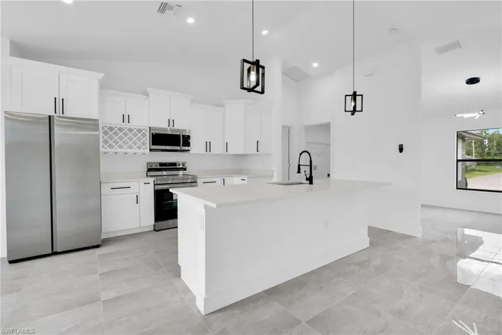 Kitchen featuring appliances with stainless steel finishes, white cabinets, a kitchen island with sink, pendant lighting, and high vaulted ceiling