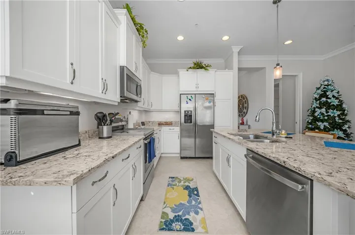 Kitchen with stainless steel appliances, white cabinets, decorative light fixtures, ornamental molding, and recessed lighting