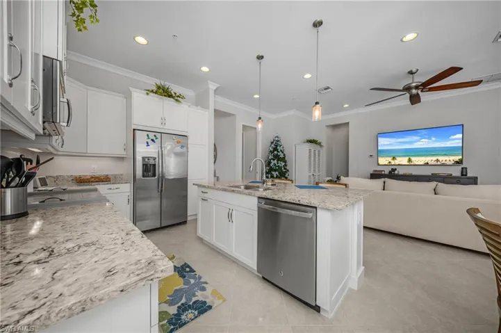 Kitchen with stainless steel appliances, crown molding, white cabinets, open floor plan, and pendant lighting