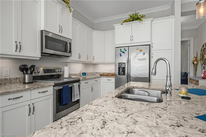 Kitchen with stainless steel appliances, white cabinetry, light stone counters, and crown molding
