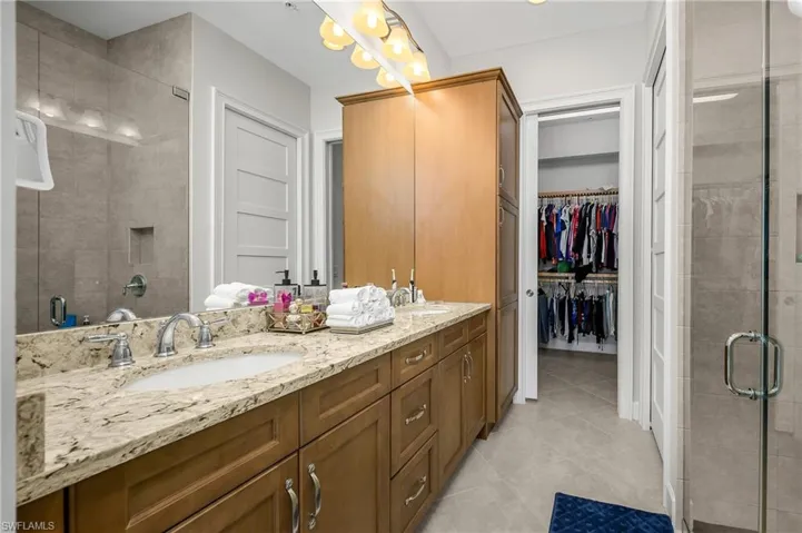 Bathroom with a shower stall, double vanity, a walk in closet, and light tile patterned floors