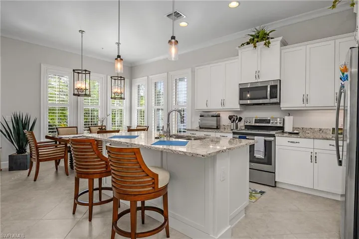 Kitchen with stainless steel appliances, white cabinets, hanging light fixtures, light stone countertops, and ornamental molding