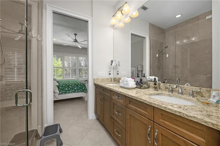 Ensuite bathroom with double vanity, a shower stall, light tile patterned floors, and recessed lighting