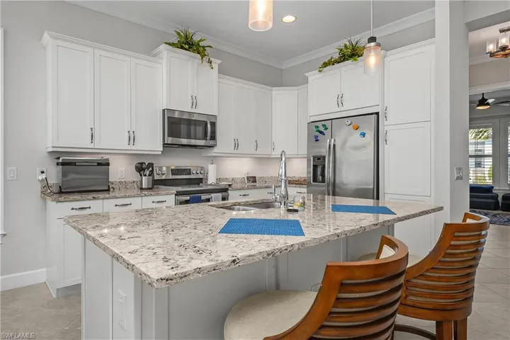 Kitchen featuring light tile patterned floors, white cabinets, a breakfast bar area, appliances with stainless steel finishes, and light stone countertops