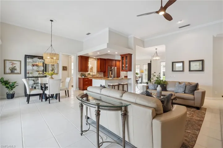 Tiled living room featuring ceiling fan with notable chandelier and crown molding