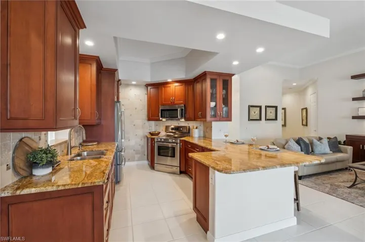 Kitchen with kitchen peninsula, light stone counters, sink, and appliances with stainless steel finishes