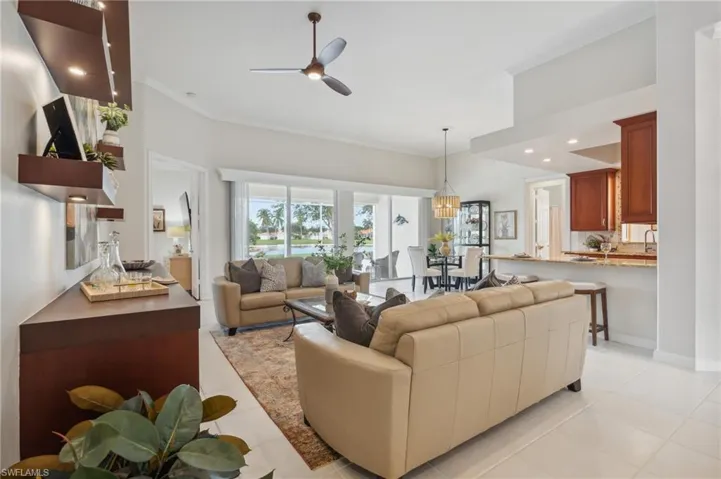 Living room featuring light tile patterned floors, ceiling fan with notable chandelier, and crown molding