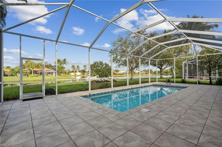 View of pool featuring a lawn, glass enclosure, a patio area, and a water view